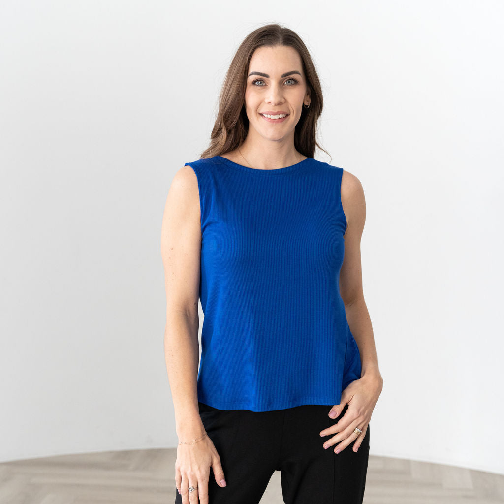 A woman wearing a blue sleeveless top with a round neckline, in a room with a white background.