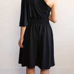Woman wearing a knee length black A-line skirt with a one shoulder black top 
