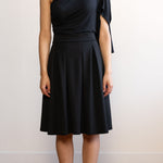 Woman wearing a knee length black A-line skirt with a one shoulder black top 