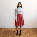 Woman wearing a knee length brick colour A-line skirt with a light grey turtleneck top