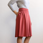 Woman wearing a knee length brick colour A-line skirt with a light grey turtleneck top