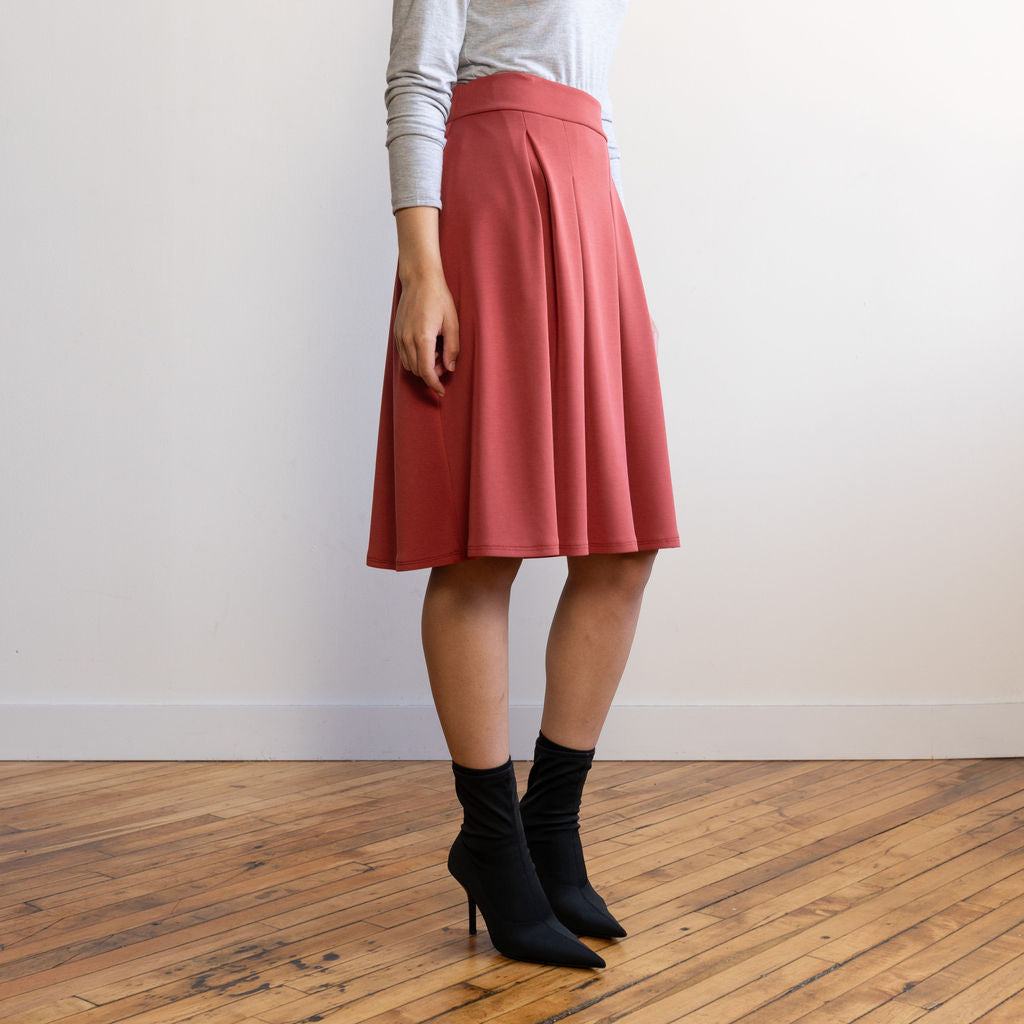 Woman wearing a knee length brick colour A-line skirt with a light grey turtleneck top