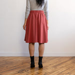 Woman wearing a knee length brick colour A-line skirt with a light grey turtleneck top