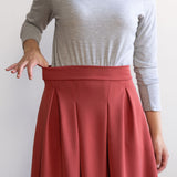 Woman wearing a knee length brick colour A-line skirt with a light grey turtleneck top