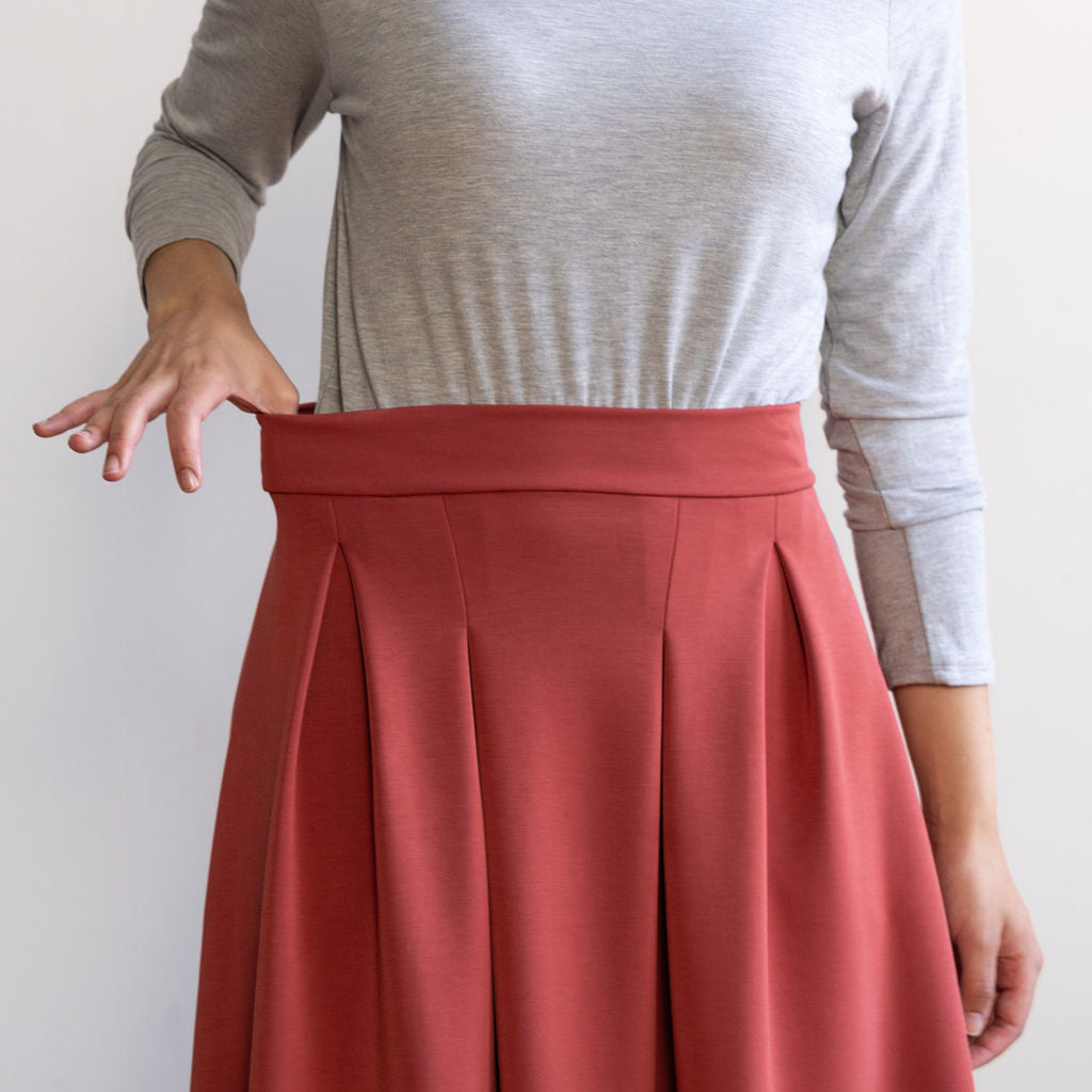 Woman wearing a knee length brick colour A-line skirt with a light grey turtleneck top