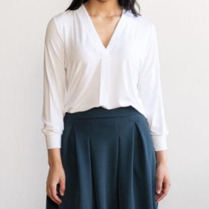 Woman wearing a loose flowing white v-neckline shirt with navy skirt