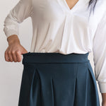 Woman wearing a knee length navy colour A-line skirt with a long sleeve v-neck white top