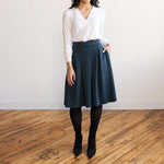 Woman wearing a knee length navy colour A-line skirt with a long sleeve v-neck white top