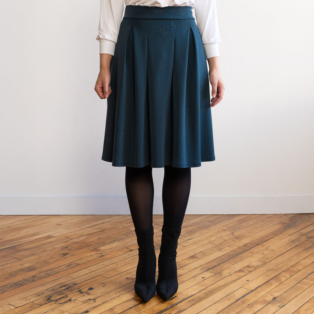 Woman wearing a knee length navy colour A-line skirt with a long sleeve v-neck white top