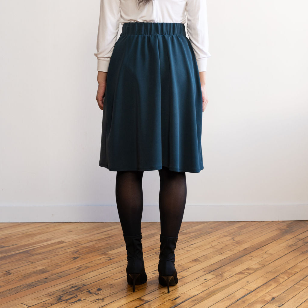 Woman wearing a knee length navy colour A-line skirt with a long sleeve v-neck white top
