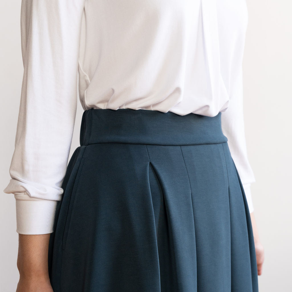 Woman wearing a knee length navy colour A-line skirt with a long sleeve v-neck white top