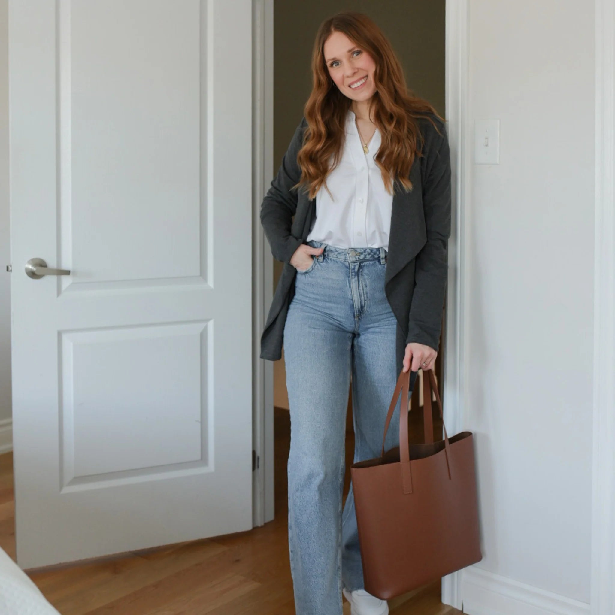 Woman wearing white long sleeve button up shirt with grey cardigan and jeans