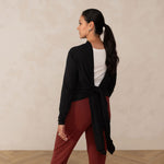 Woman wearing long sleeve black cardigan knotted at the back with white v-neckline shirt and red relaxed pants