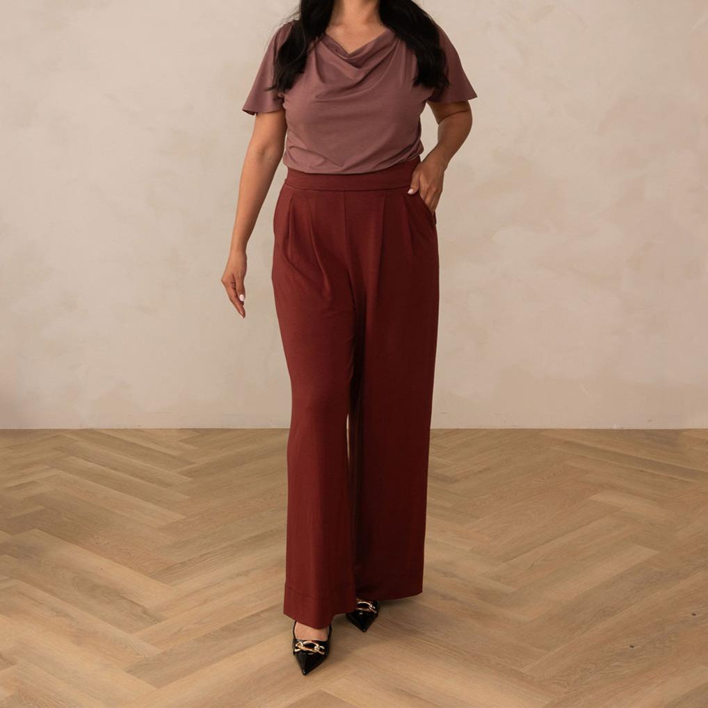 woman wearing a deep mauve cowl neck top with red high waisted pants