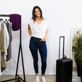 Woman standing next to a black suitcase in a room with a clothing rack and plant.