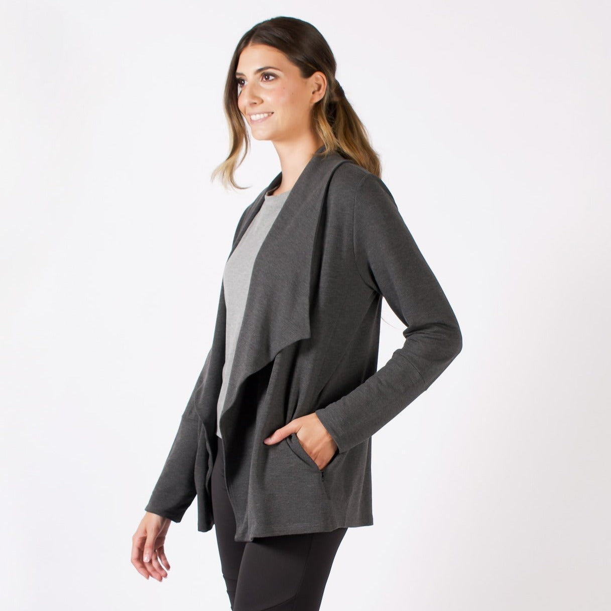 Woman wearing grey open loose cardigan with wide flowing lapel and pockets with a light grey shirt and black leggings