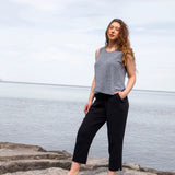 Woman standing on rocks by a body of water wearing a gray tank top and black pants.
