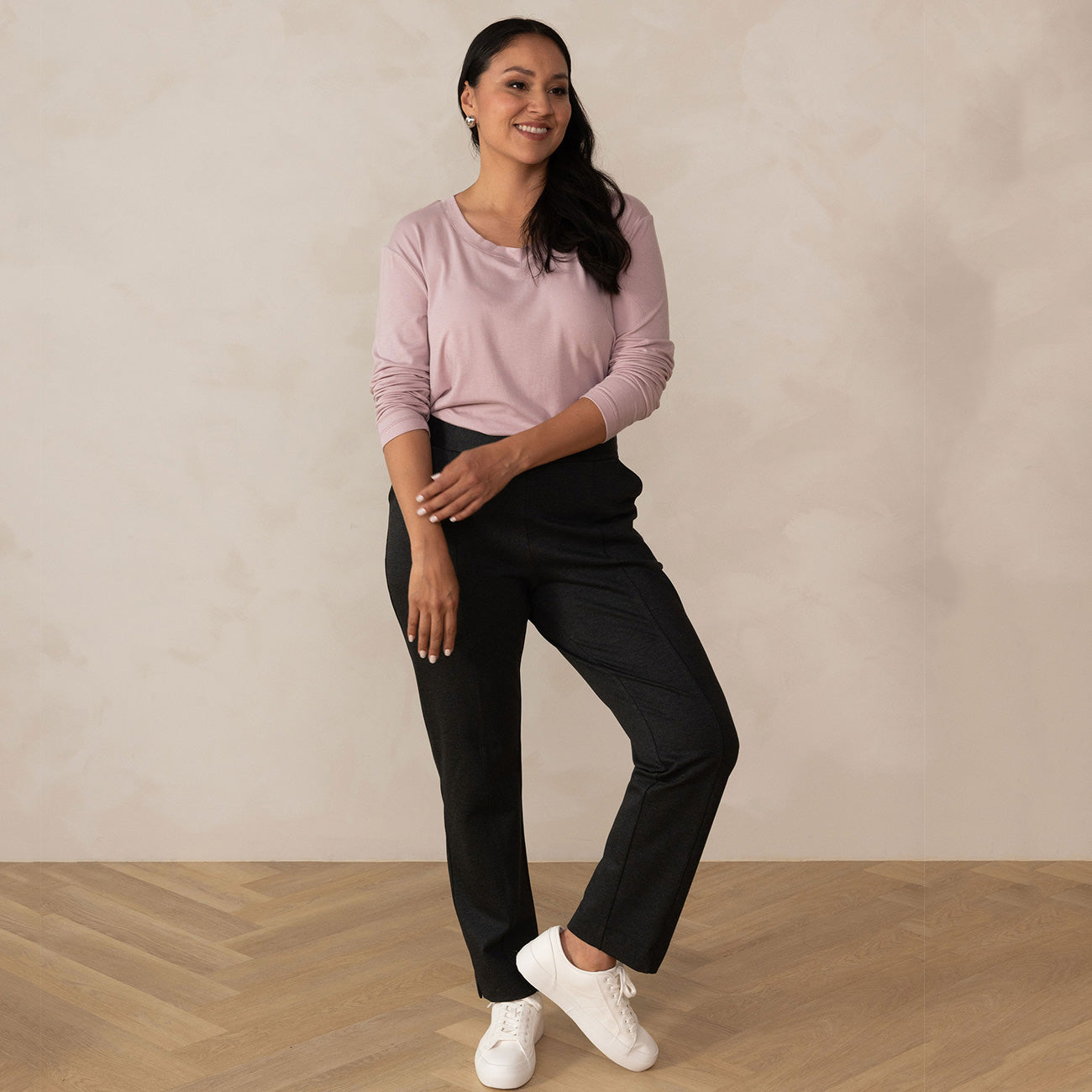 woman wearing a long sleeve scoop neck light pink top paired with tailored grey pants and white sneakers