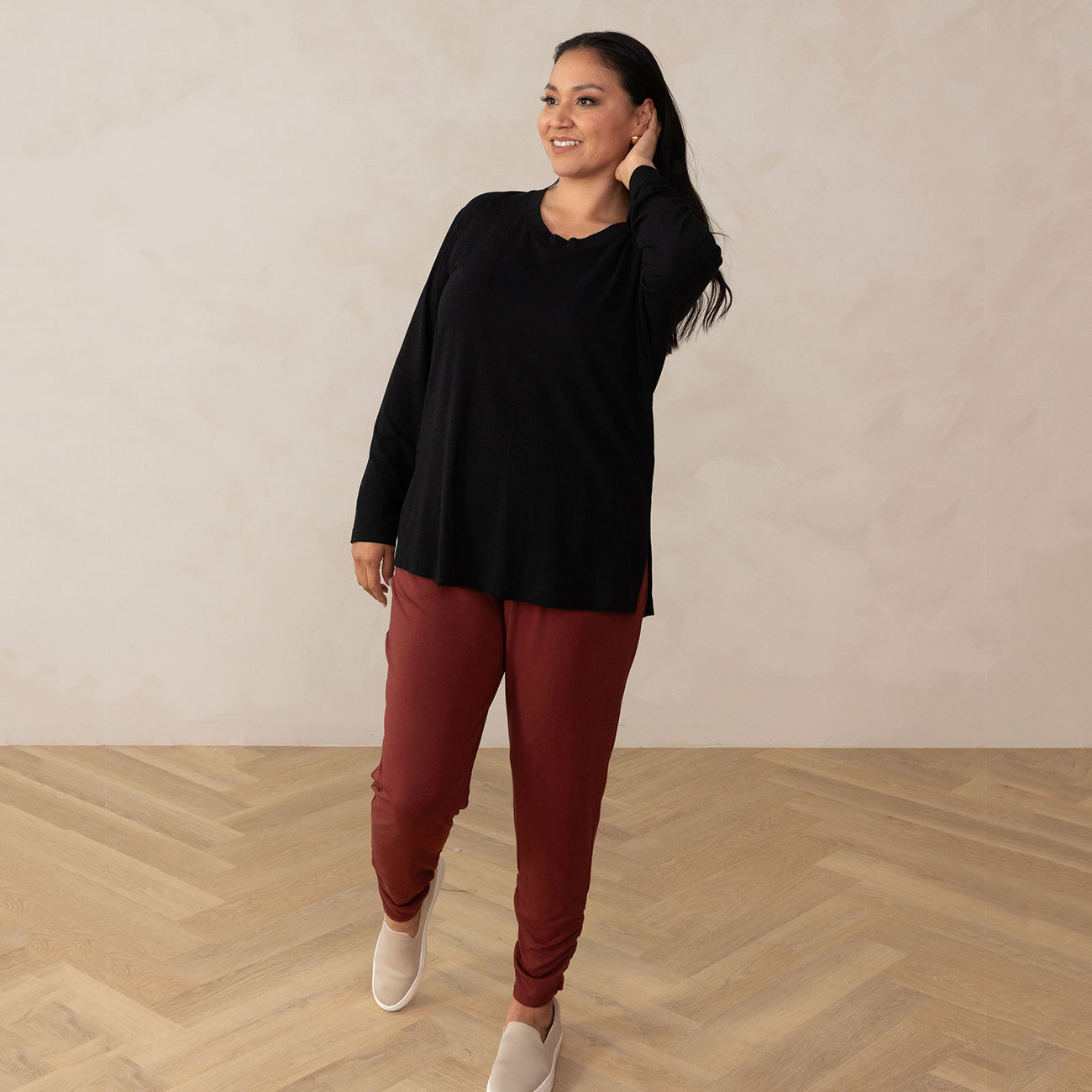 woman wearing a long sleeve scoop neck black top paired with red pants and beige sneakers