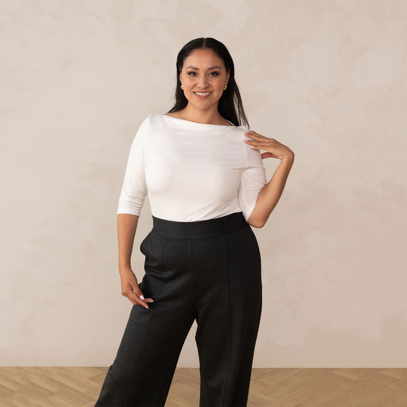 woman wearing a white boat neck blouse with tailored grey pants and golden earrings