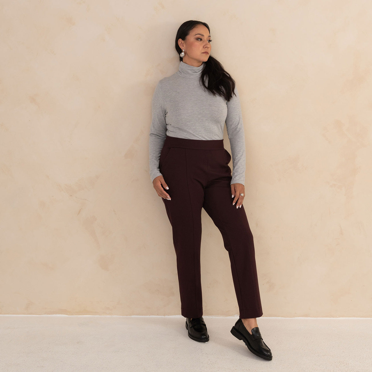 woman wearing light grey turtleneck and aubergine high waisted tailored pants with black loafers