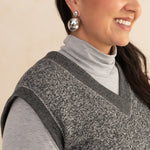 woman wearing a heirloom grey vest and a light grey turtleneck with silver earrings