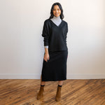 woman wearing a black v-neck long-sleeve sweater with a matching midi skirt in the same black fabric and brown boots