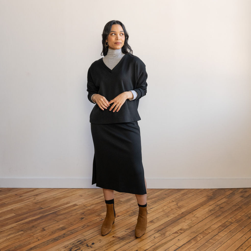 woman wearing a black v-neck long-sleeve sweater with a matching midi skirt in the same black fabric and brown boots