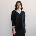 Woman wearing a grey turtleneck longlseeve blouse with a black v-neck sweater layered on top