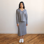 woman wearing a grey v-neck long-sleeve sweater with a matching midi skirt in the sabe heathered grey fabric and white shoes