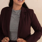 woman smiling and wearing an aubergine blazer paired with a stripes boat neck