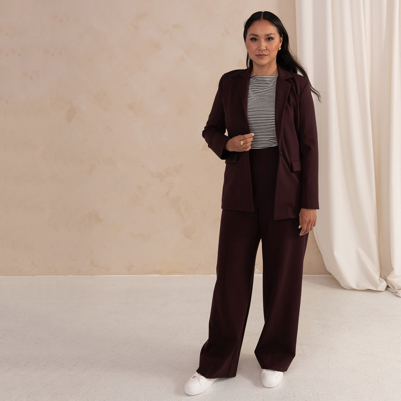 woman wearing an aubergine blazer with a boat neck stripes top and a golden earring and ring