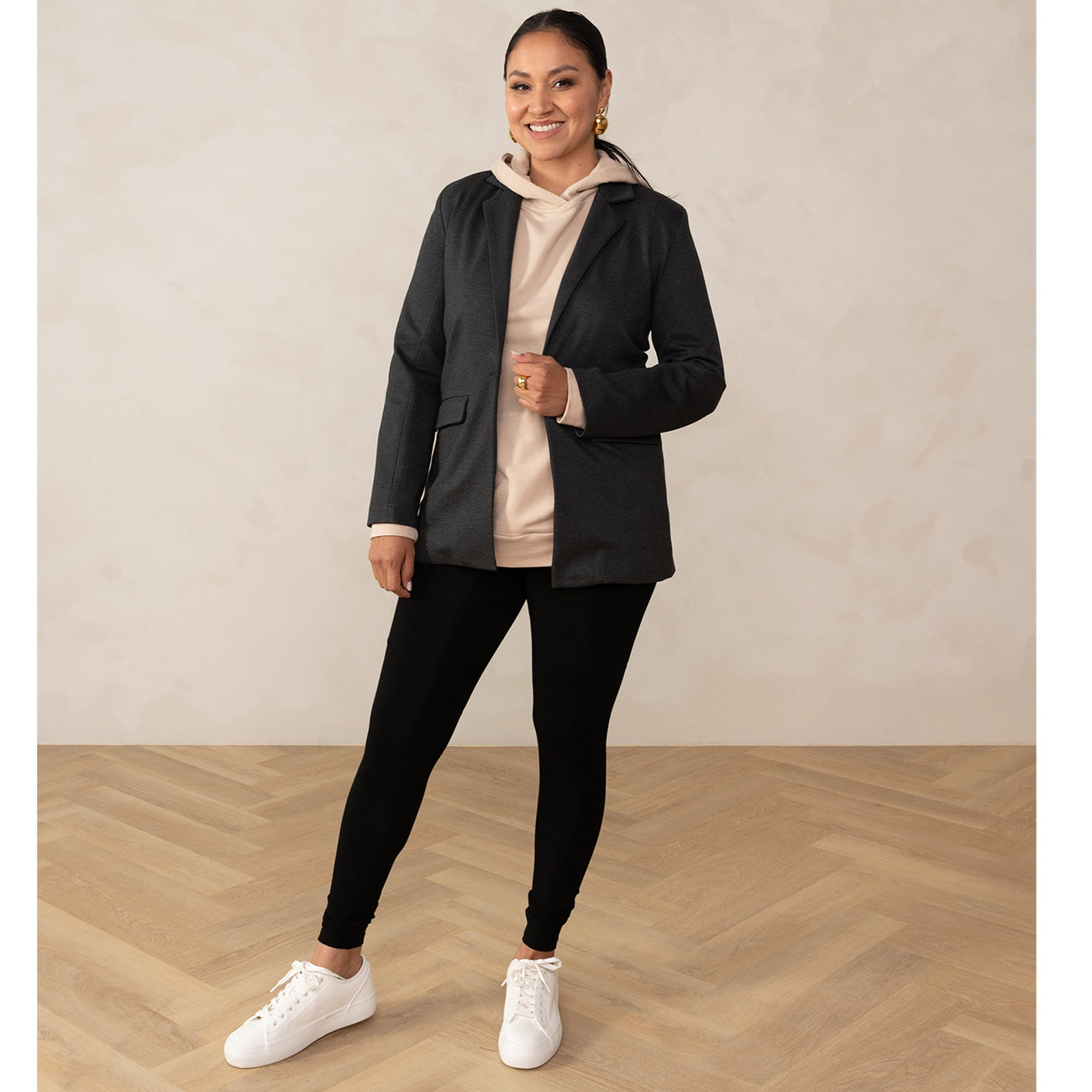 woman wearing a grey blazer on top of a sand coloured hoodie paired with black leggings and white sneakers