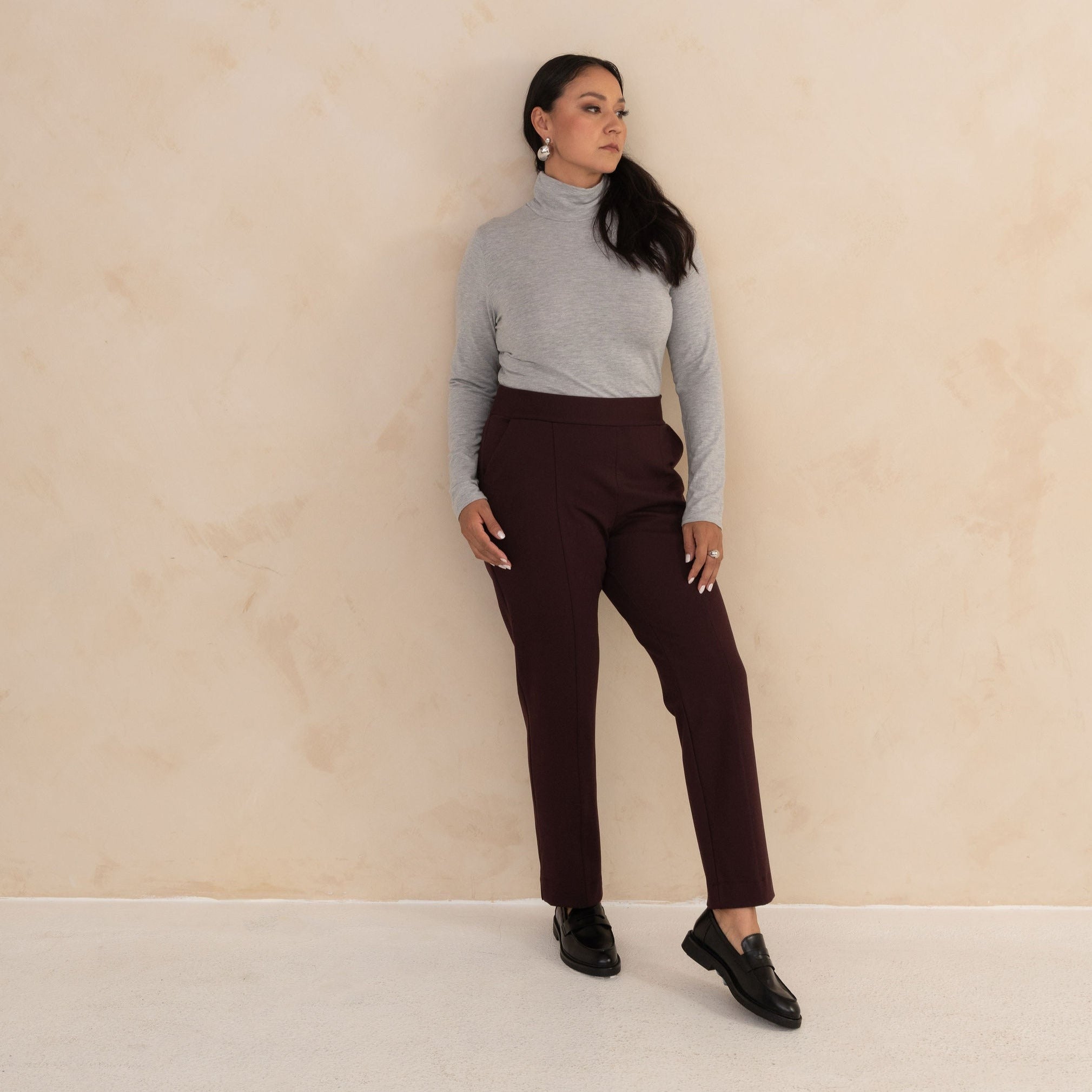 woman wearing a light grey longsleeve turtleneck and tailored navy pants with black loafers