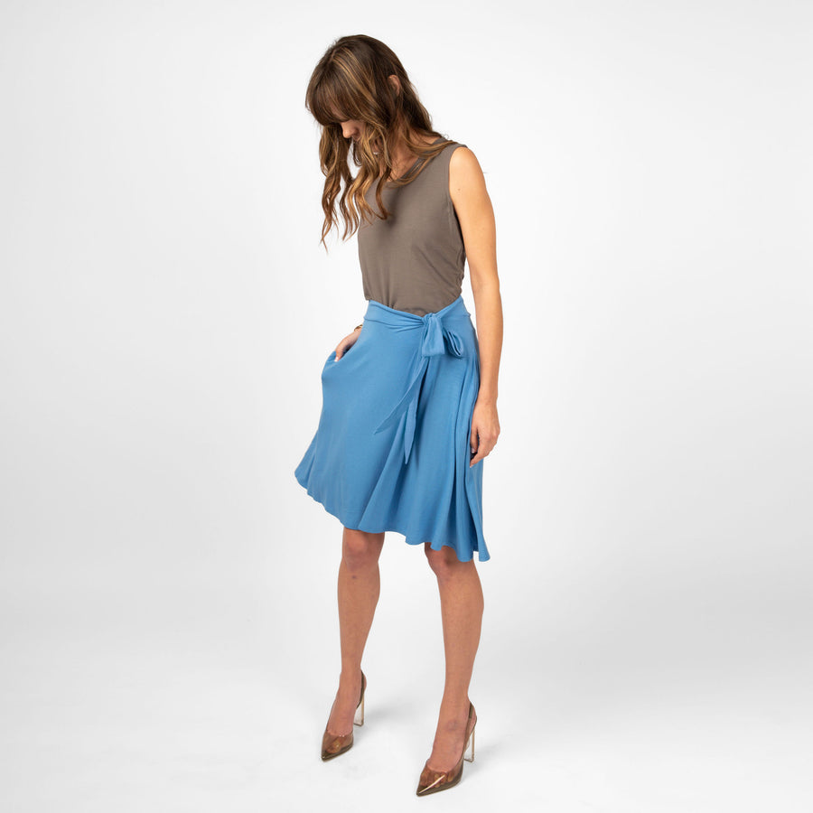 Woman wearing sky blue knee length stretchy wrap skirt with pockets and side bow with brown sleeveless shirt