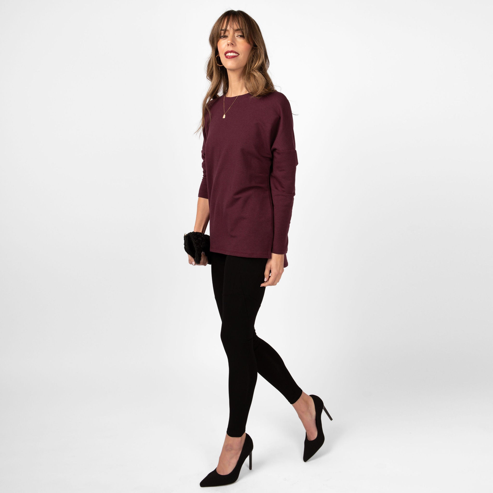 Woman wearing black form fitting stretchy leggings with a maroon long sleeve sweatshirt