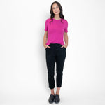 Woman wearing black tailored stretchy ankle length pants paired with loose pink scoop neckline shirt