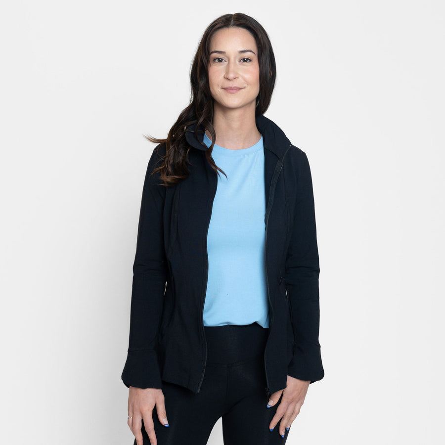 Woman wearing fitted navy stretchy front zippered jacket open with blue v-neckline shirt with black fitted leggings