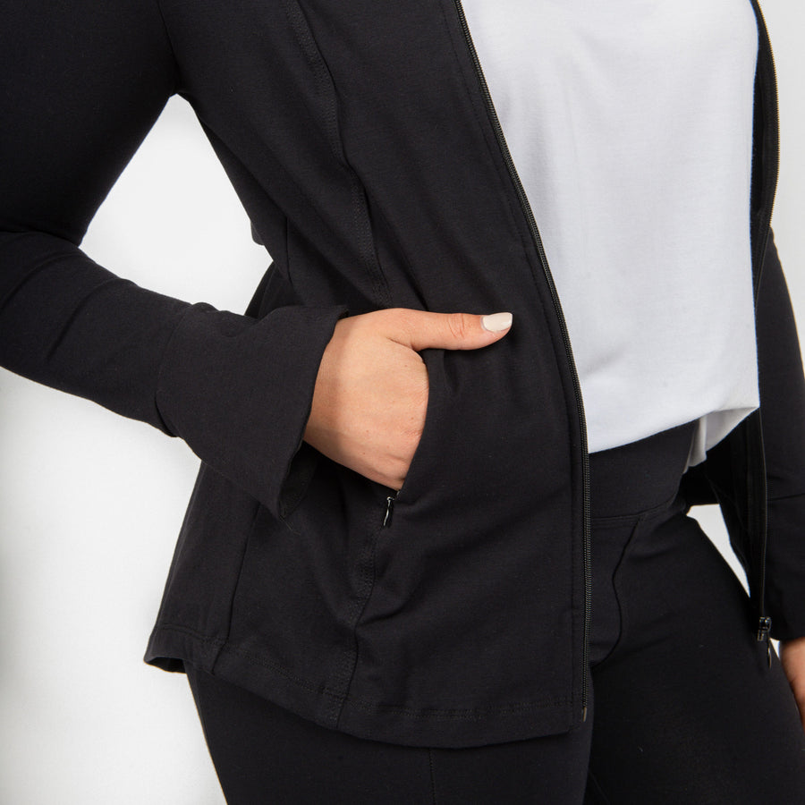 Woman wearing fitted navy stretchy front zippered jacket open featuring pockets with white shirt and black fitted leggings