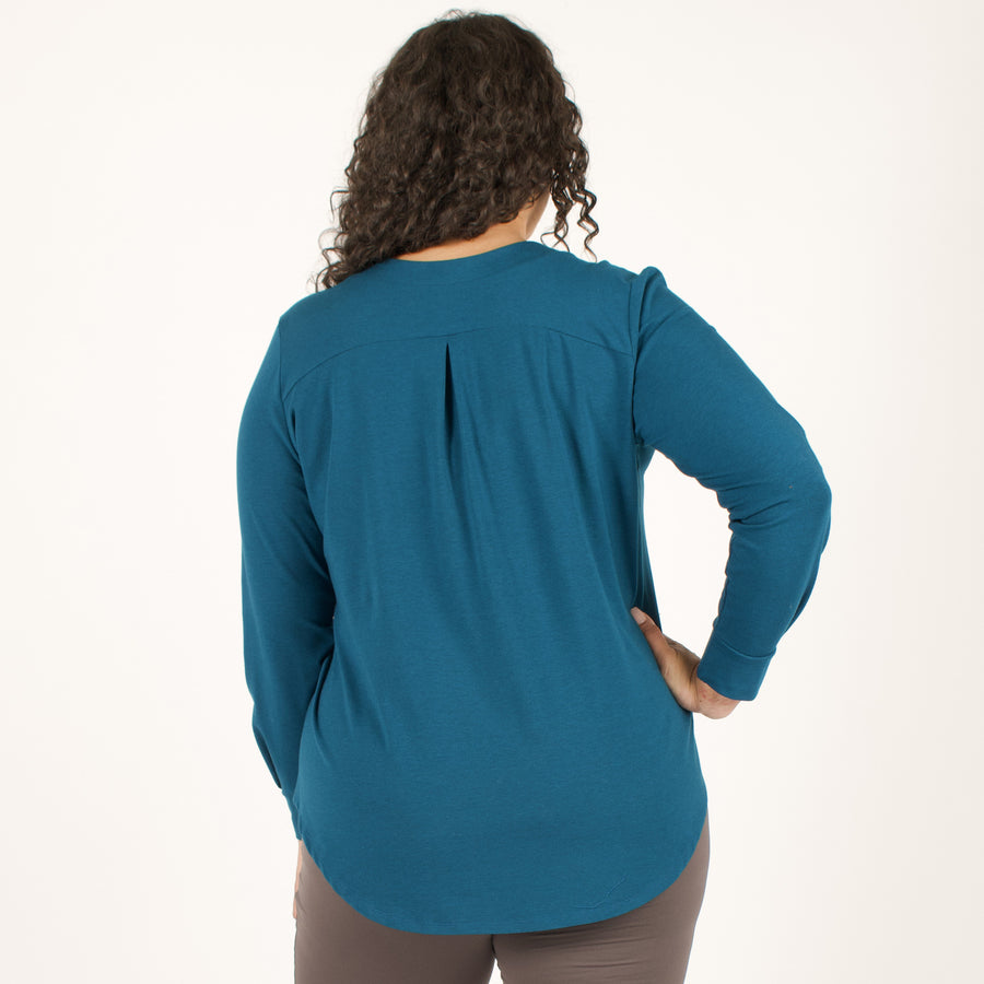 Woman wearing bright blue long sleeve button up shirt with brown fitted leggings