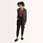 Woman wearing cherry red form fitting long sleeve reversible top with either a scoop neckline or horizontal neckline paired with black fitted sweatpant and grey loose open cardigan 
