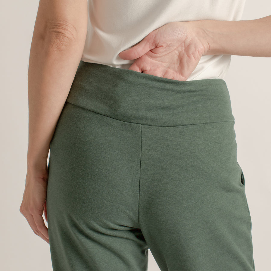 Woman wearing green stretchy sweatpants featuring back horizontal pocket at the waistband with white shirt
