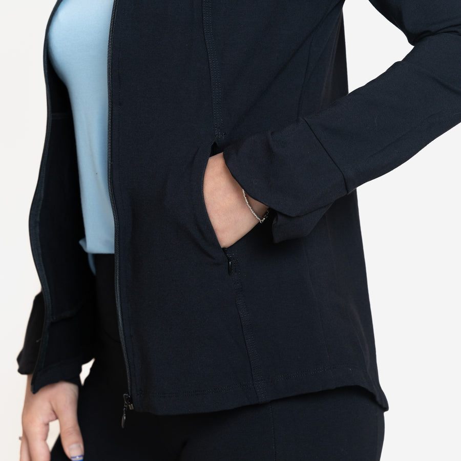 Woman wearing fitted navy stretchy front zippered jacket open featuring pockets with light blue shirt and black fitted leggings