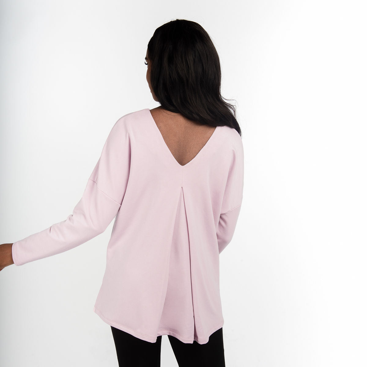 Woman wearing light pink long sleeve shirt with a relaxed fit, front scoop neckline or v-neckline back with pleating and side slits paired with black fitted leggings