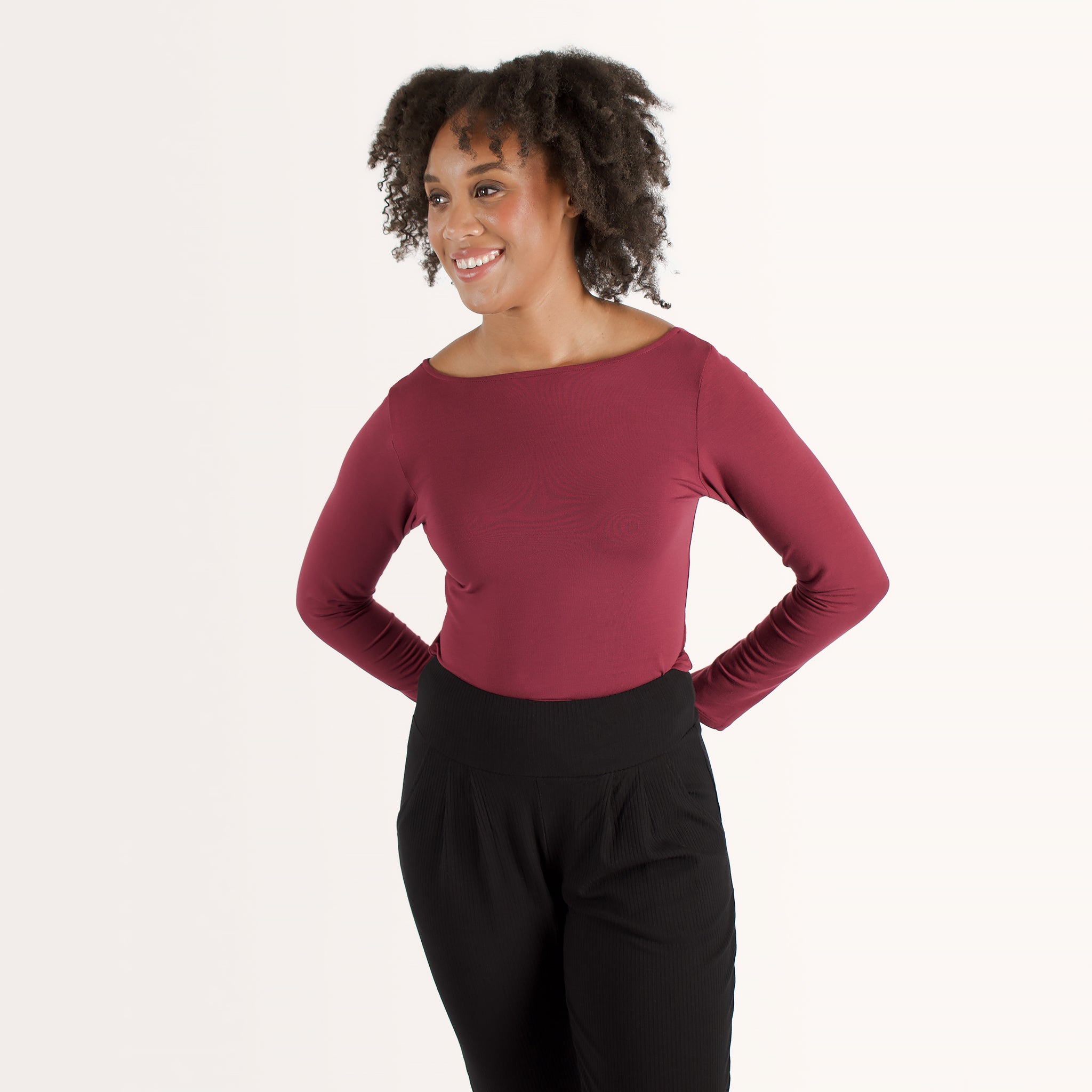 Woman wearing cherry red form fitting long sleeve reversible top with either a scoop neckline or horizontal neckline paired with black fitted sweatpant
