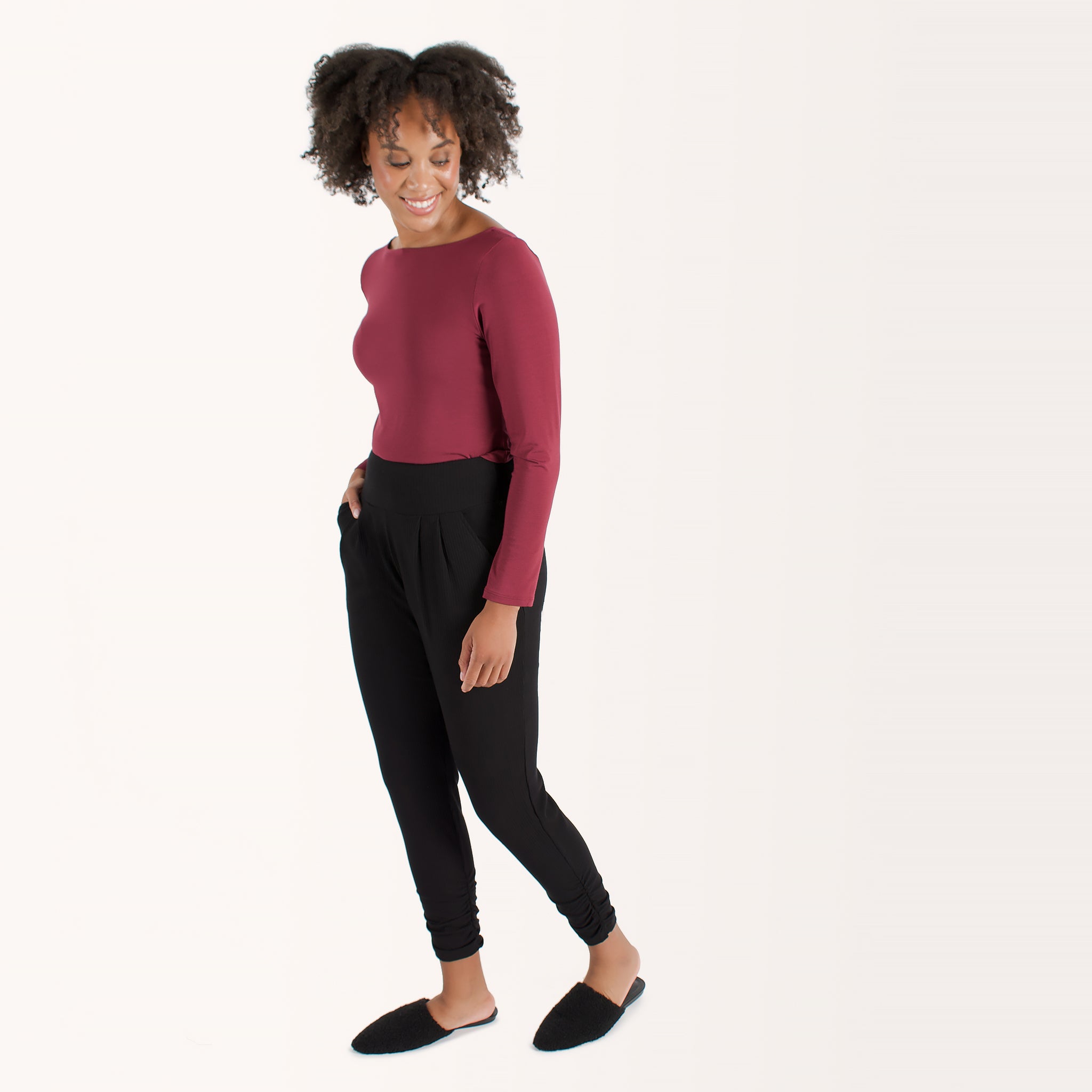 Woman wearing cherry red form fitting long sleeve reversible top with either a scoop neckline or horizontal neckline paired with black fitted sweatpant