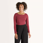 Woman wearing cherry red form fitting long sleeve reversible top with either a scoop neckline or horizontal neckline paired with black fitted sweatpant