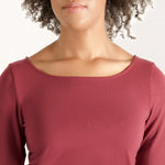 Woman wearing cherry red form fitting long sleeve reversible top with either a scoop neckline or horizontal neckline