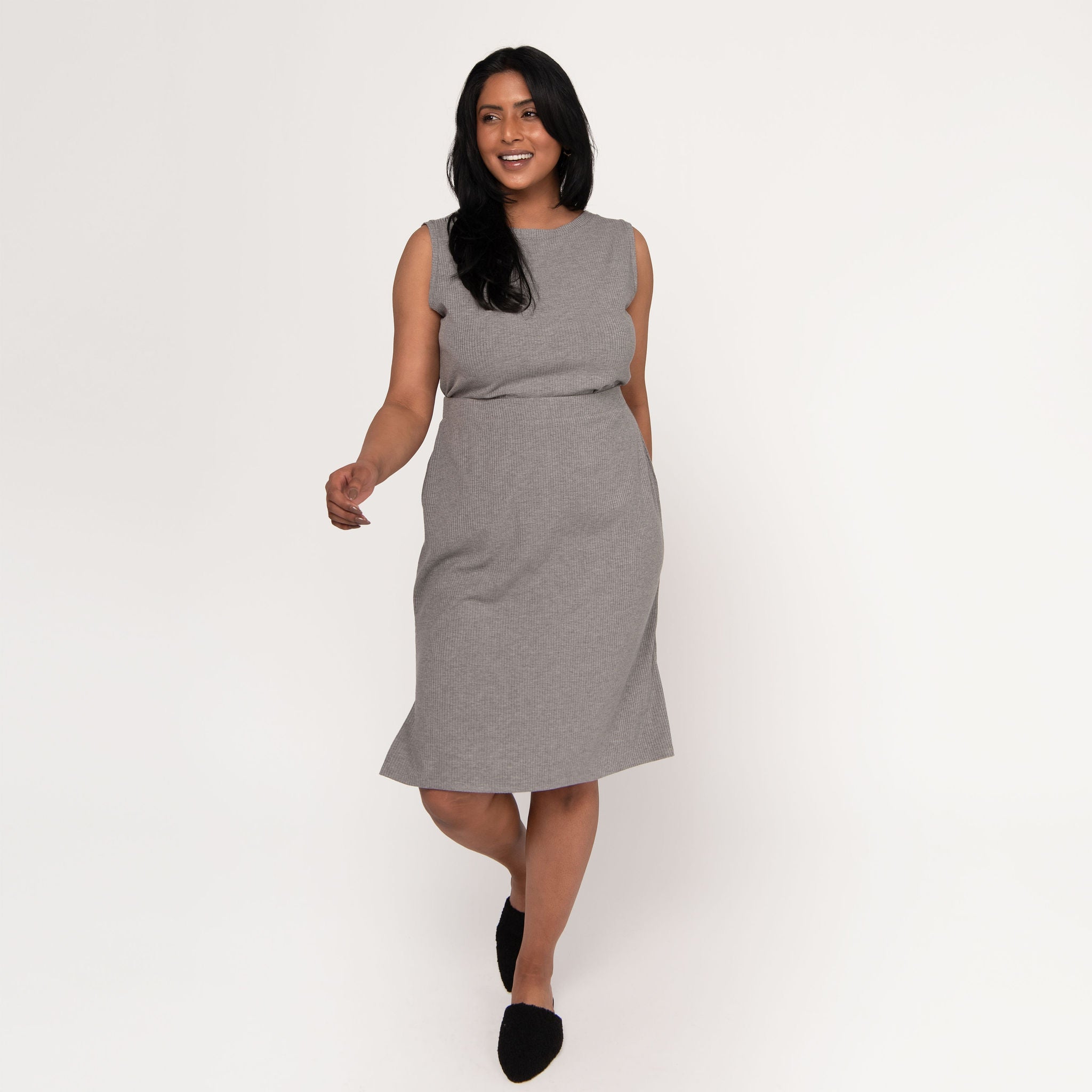  Woman wearing grey body-skimming fit stretchy mid calf length vertical ribbed skirt with tucked in grey sleeveless shirt