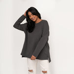 Woman wearing light grey long sleeve shirt with a relaxed fit, front scoop neckline or v-neckline back  with pleating and side slits paired with white torn jean